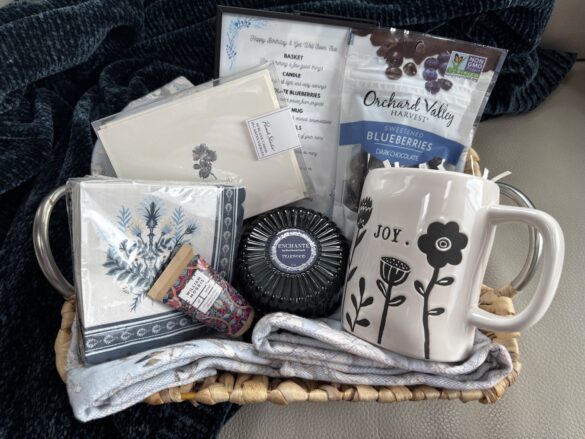 woven basket filled with mug, candle, tea towels, stationery, and chocolate covered blueberries
