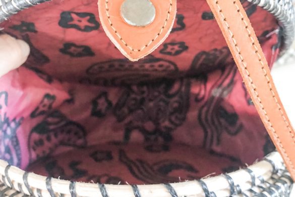 Inside of round rattan purse showing red batik fabric lining with star and elephant pattern, and tan leather closure strap