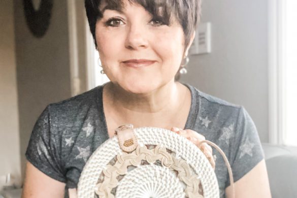 Deborah Bass smiling and holding a handmade round rattan purse with a light tan pattern, seated indoors in natural light