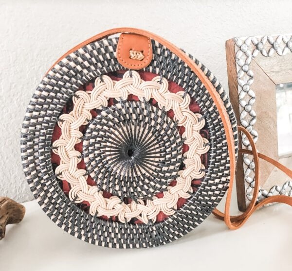 Round woven rattan purse with orange leather strap and batik lining, placed on a white surface