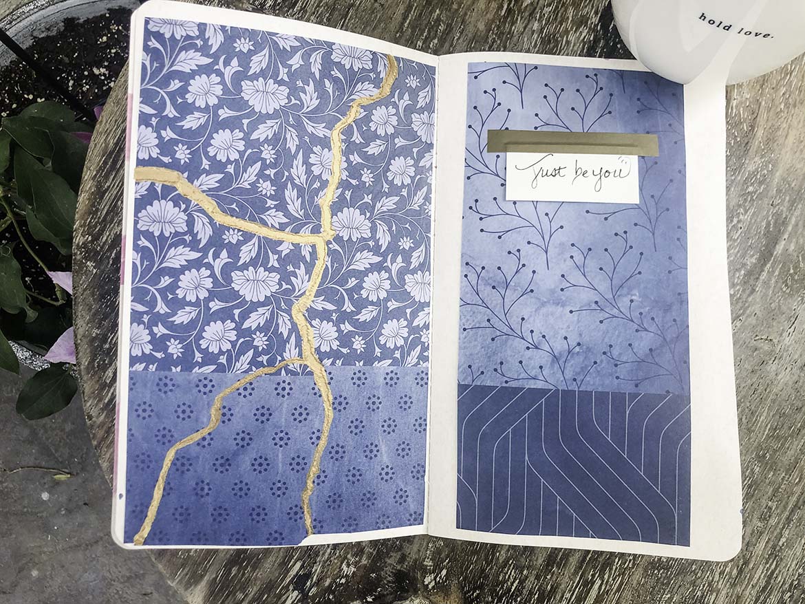An open art journal displays torn blue flowered paper with a vein of gold through it as well as a mix of blue patterns with a handmade sign that reads: Just Be You
