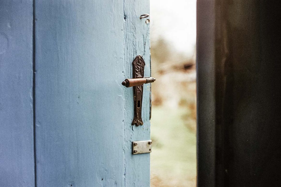 An old barn door painted turquoise is slightly open to a bright outdoors