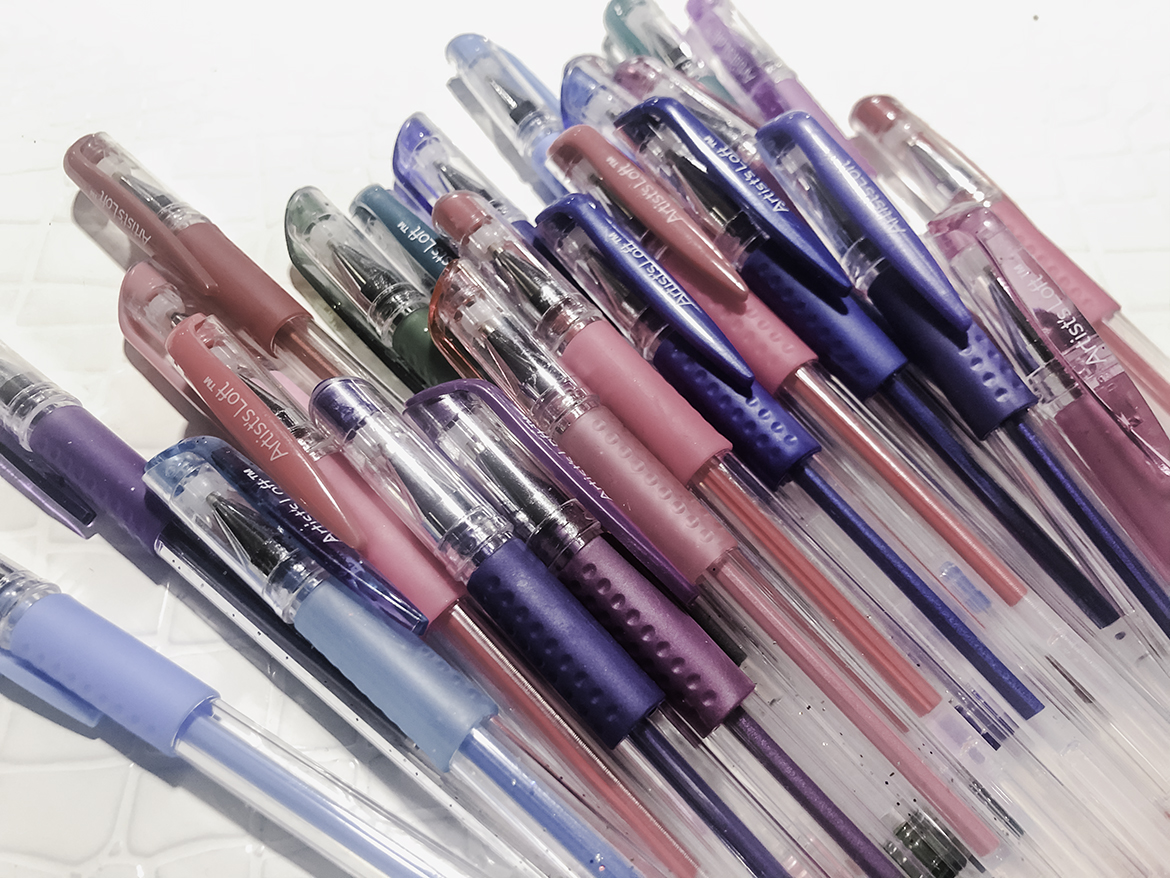 Dozens of gel pens in various, vivid color lay on a bright white background.
