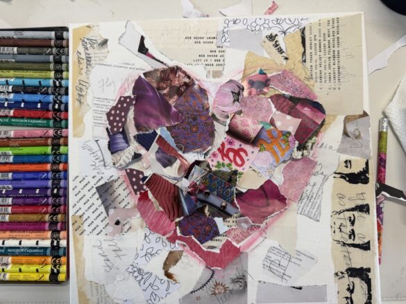 Various torn papers glued to a board with colorful pastel crayons on a table.