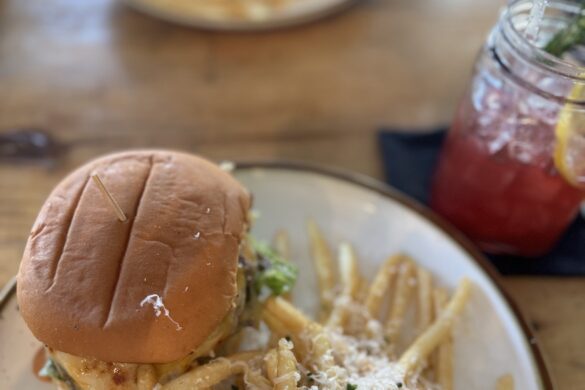 A dinner plate with a hamburger and truffle fries with curly Parmesan cheese just served at a wooden table