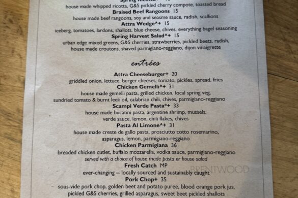 A paper menu with starters, entrees, sides and dessert is laid on a wood table.