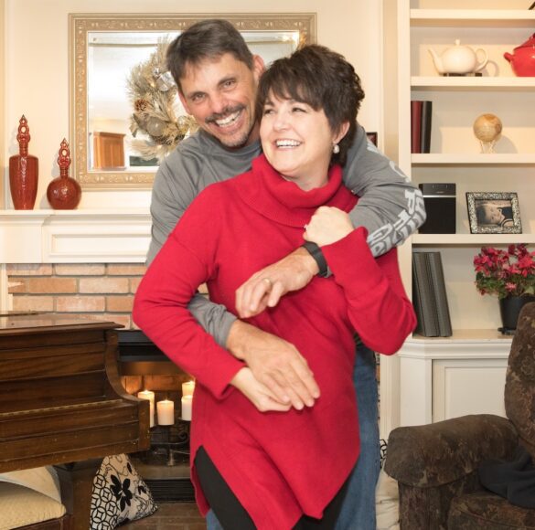 A man playfully hugs a woman from behind as they prepare to take a picture at Christmas