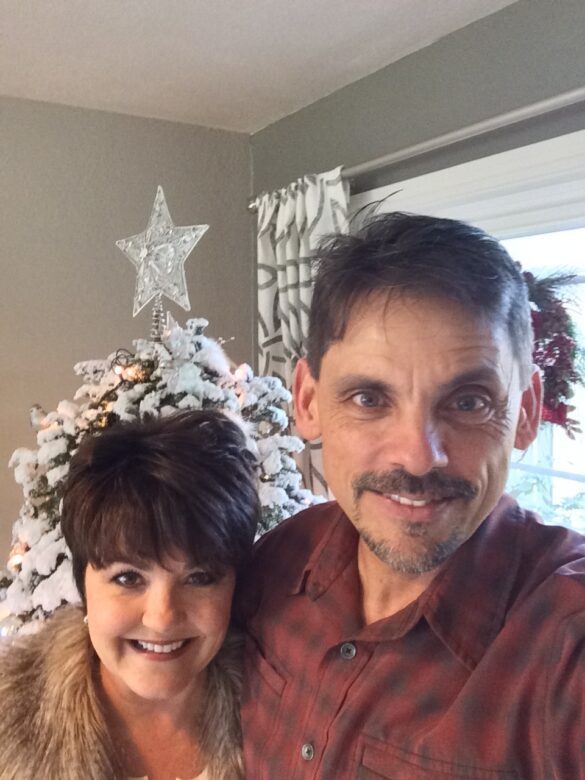 A smiling, happy couple in front of an all white, flocked Christmas tree with a star on top take a selfie