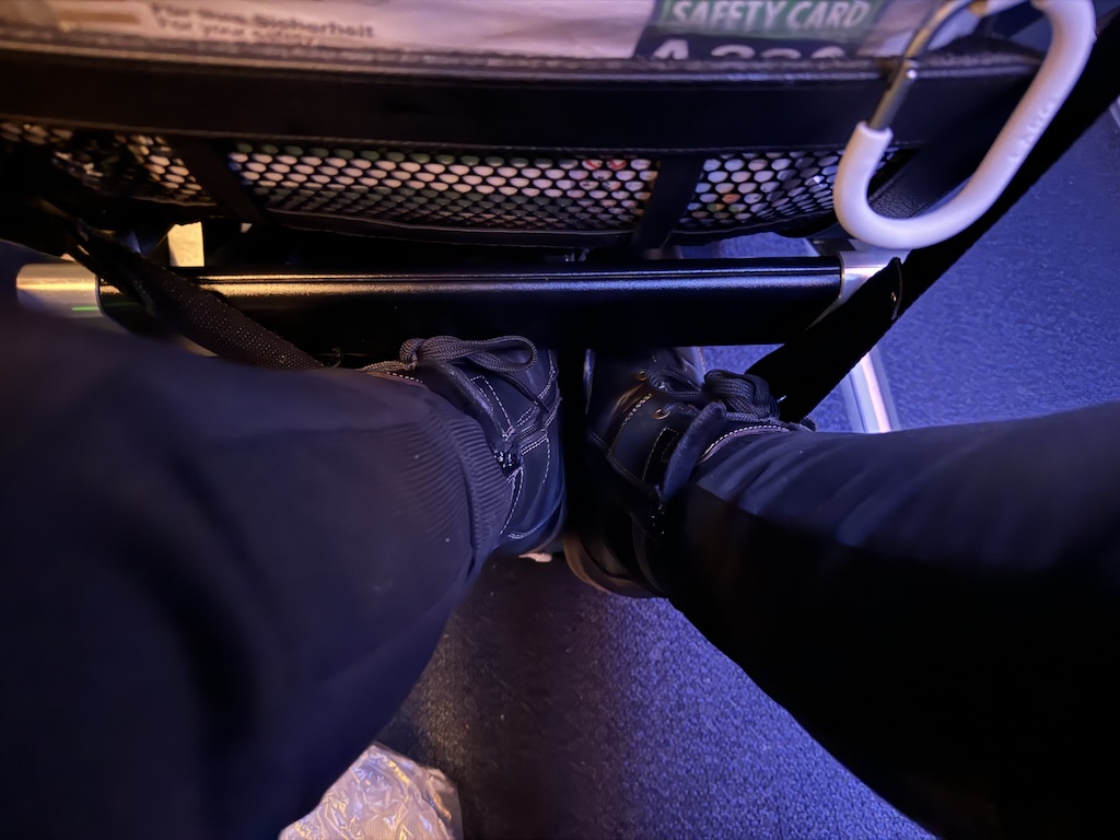 Feet resting in a hanging footrest on an airplane, tray table above