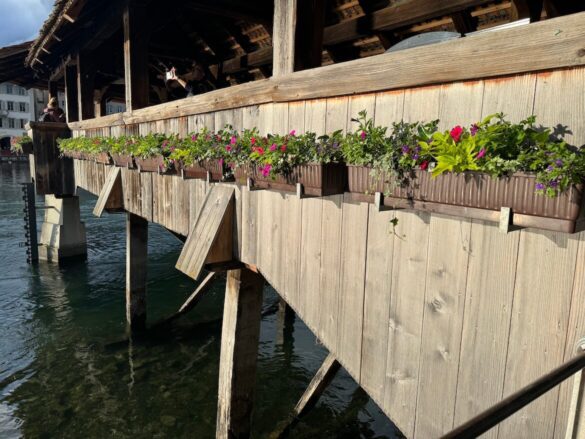 Overflowing flower boxes with red, pink, and white summer blooms along the wooden railing of Chapel Bridge in Lucerne, Switzerland