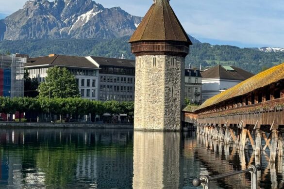 Stone Water Tower and wooden Chapel Bridge reflecting in the Reuss River, with Mount Pilatus in the background in Lucerne, Switzerland