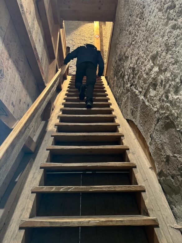 A person climbing a steep wooden staircase inside a Musegg Wall tower in Lucerne, Switzerland