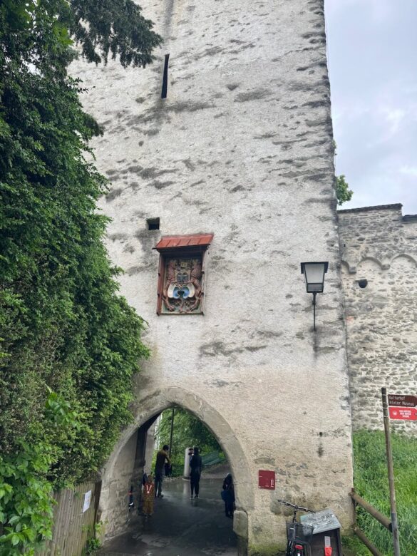 Stone archway beneath Männli Tower along Lucerne’s Musegg Wall, with a coat of arms relief above the entrance and people walking underneath