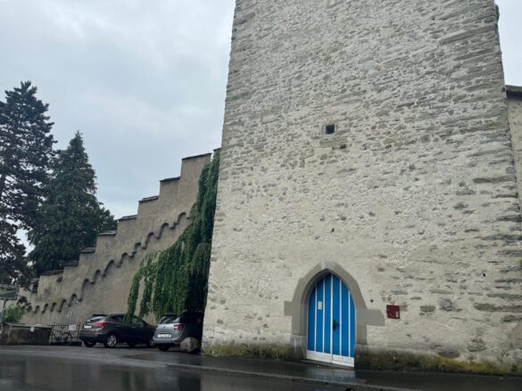 Schirmer Tower and adjacent stepped battlements of the Musegg Wall in Lucerne, with parked cars in front and homes nearby