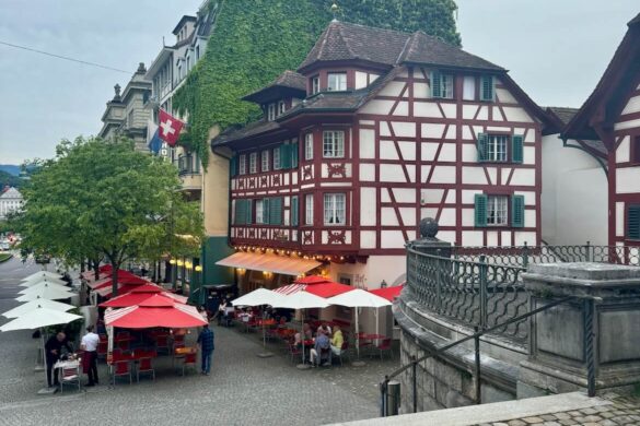 Historic half-timbered Hotel Rebstock in Lucerne, Switzerland, with red and white exterior and outdoor café seating beneath colorful umbrellas