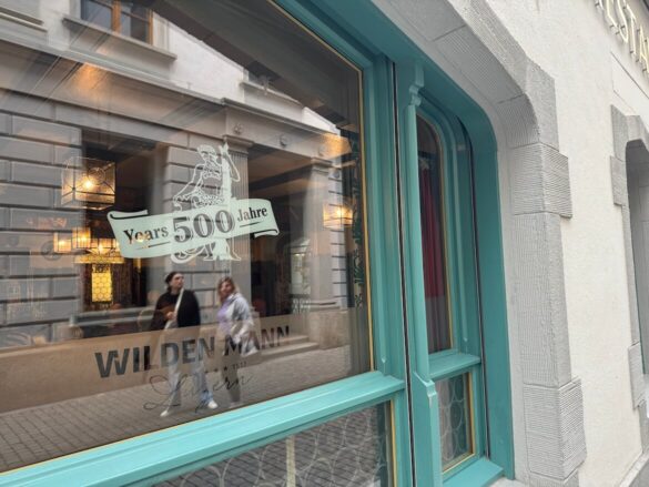 Window of Hotel Wilden Mann in Lucerne with reflection of passersby and signage celebrating 500 years since its founding in 1517