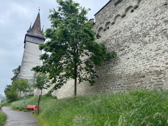 View of Musegg Wall and tower in Lucerne with a red bench below, showing the scale of the medieval fortress walls