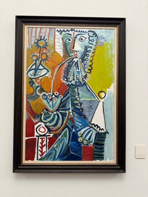 Colorful abstract Picasso painting of a seated man holding a pipe and a bouquet of flowers, rendered in bold geometric shapes and lines.