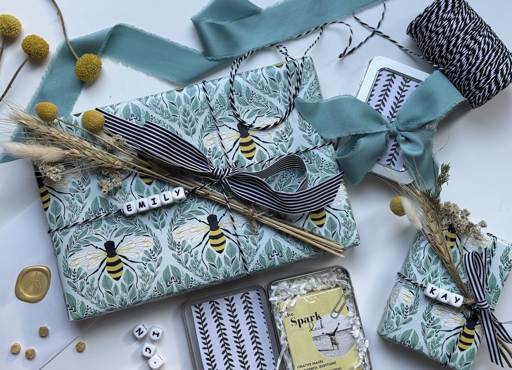 Wrapped Spark Cards gifts with bee-patterned paper, ribbon, and dried floral details, styled by Deborah Bass