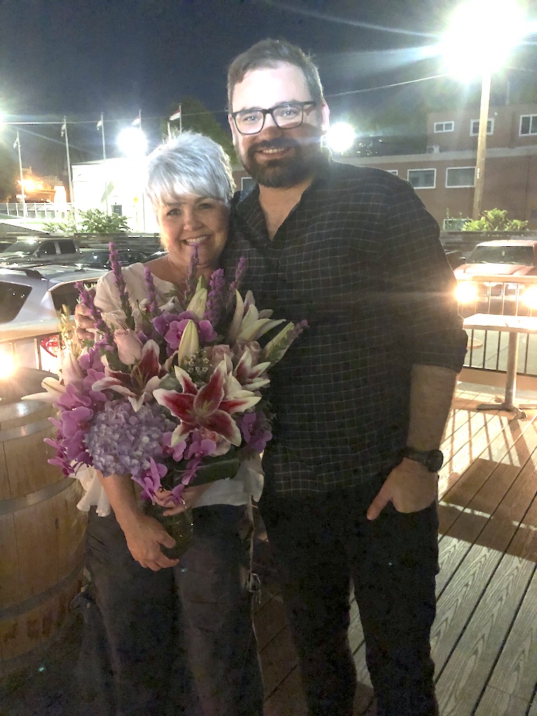 Deborah holding a large, colorful floral arrangement with her son Brandon for her 60th birthday celebration, nearly three years ago