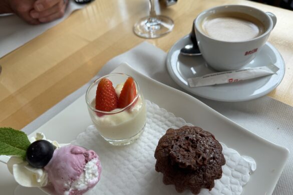 Plate with panna cotta topped with strawberries, chocolate cake, and gelato, with cappuccino in the background