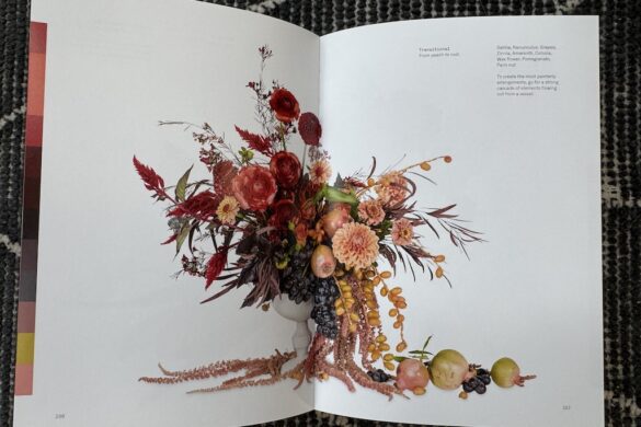Floral arrangement in a white urn with dahlias, ranunculus, zinnias, grapes, and other flowers in a peach-to-rust palette, cascading with fruit, page 266.