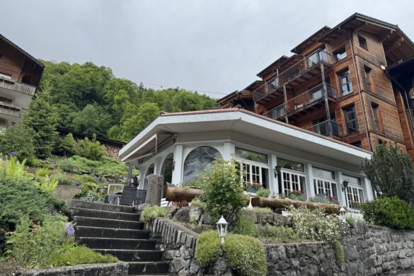 Silberhorn White restaurant with large windows and flower boxes built into a hillside, stone steps leading up, surrounded by wooden chalets and green trees