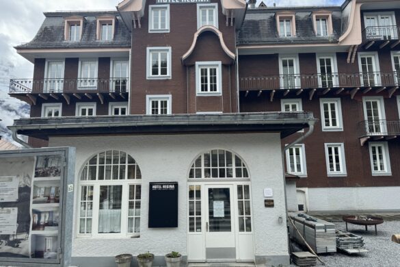 Facade of the Hotel Regina in Mürren with arched windows, balconies, and brown timber exterior under shifting clouds