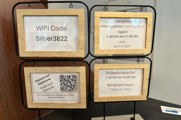 Set of four wooden-framed signs at Hotel Silberhorn reception desk showing WiFi code, reception hours, breakfast hours, and guest card QR code