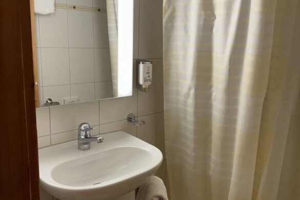Compact hotel bathroom with white sink, mirror, and cream shower curtain at Hotel Silberhorn in Lauterbrunnen, Switzerland