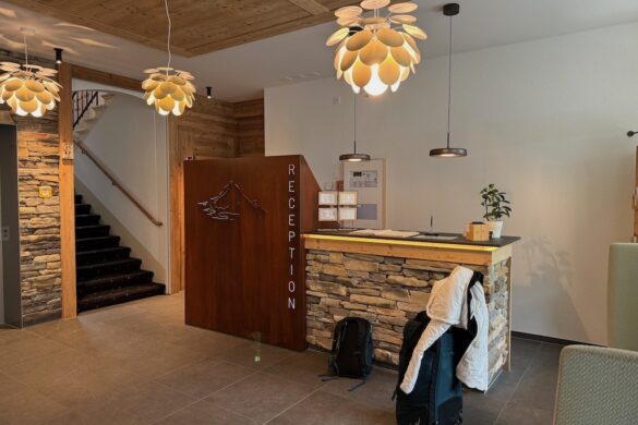 Reception area at Hotel Silberhorn in Lauterbrunnen with stone and wood finishes; luggage and a backpack sit in front of the desk beneath modern pendant lights.