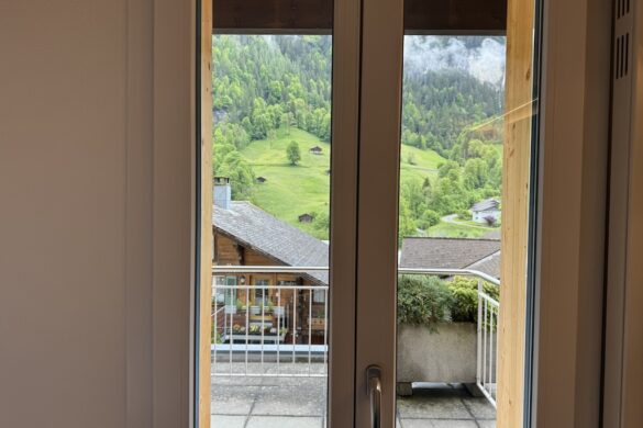 Hotel window open to a balcony with rooftops and green hills in Lauterbrunnen, Switzerland