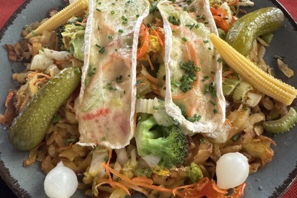 Plate of rösti potato dish topped with grilled vegetables, pickles, and melted cheese, served at Restaurant Schützen in Lauterbrunnen