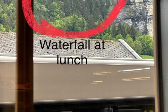 View through a restaurant window toward a tall waterfall cascading down a cliff in Lauterbrunnen, Switzerland