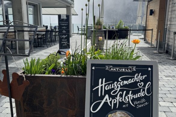 Sidewalk sign for homemade apple strudel with vanilla sauce outside a café in Mürren; tulips and misty peaks in the background