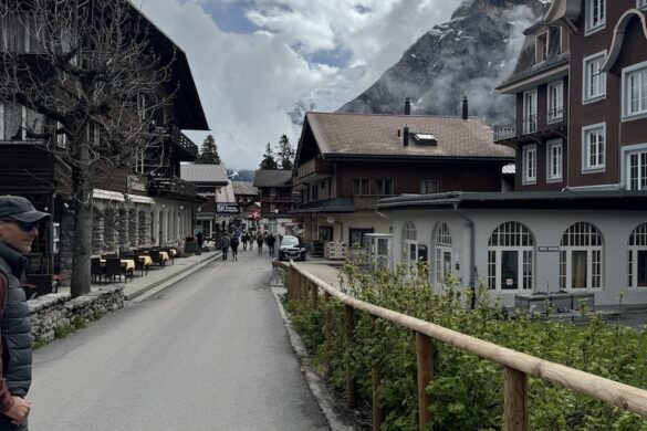 Village street in Mürren lined with chalets and cafés, Hotel Regina ahead, clouds gathering over the mountains
