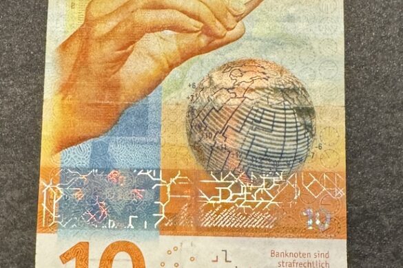 Front of the yellow Swiss 10 franc banknote showing a hand holding a conductor’s baton over a globe