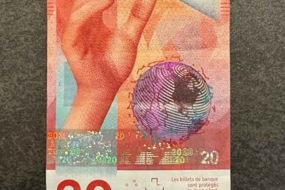 Front of the red Swiss 20 franc banknote featuring a hand holding a prism dispersing light and a globe design