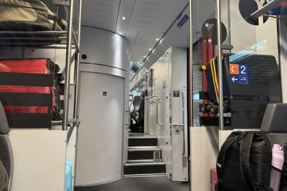 Interior of a Swiss train with overhead luggage racks, a curved wall for the restroom, and modern seating
