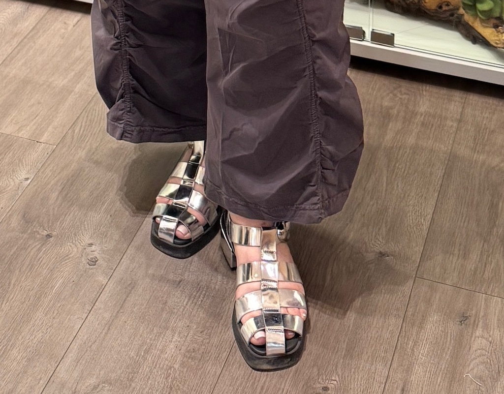 Silver metallic Aerosoles sandals worn with black pants on wood flooring