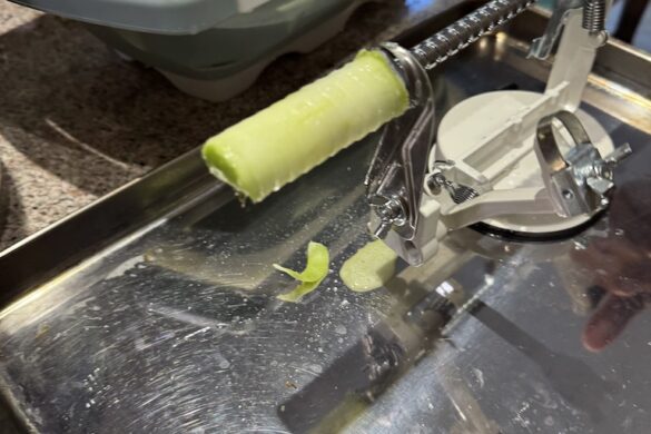 Apple core resting on an apple peeler beside a bowl of whole green apples