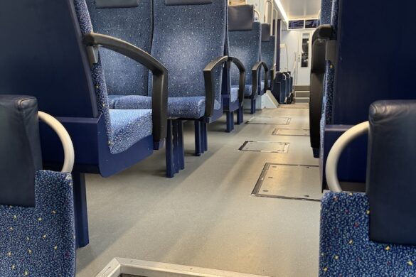Interior of a Swiss train from Lauterbrunnen to Basel, showing blue seats, clean modern design, and a window view of green hills blurred by rain