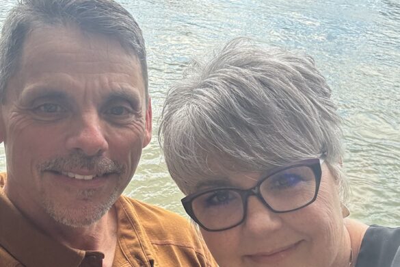 Ron and Deborah smiling with the river behind them on a sunny day