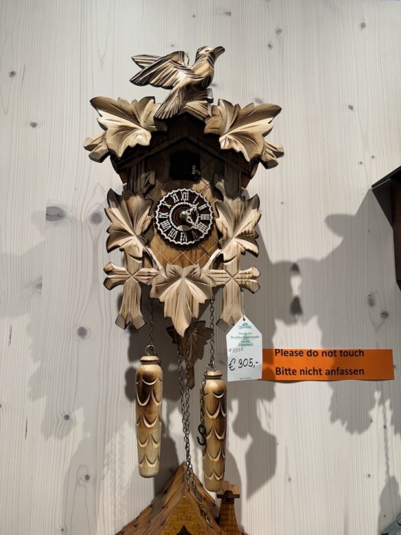 Hand-carved wooden cuckoo clock with pine cone weights and leaf designs displayed in a Black Forest shop.