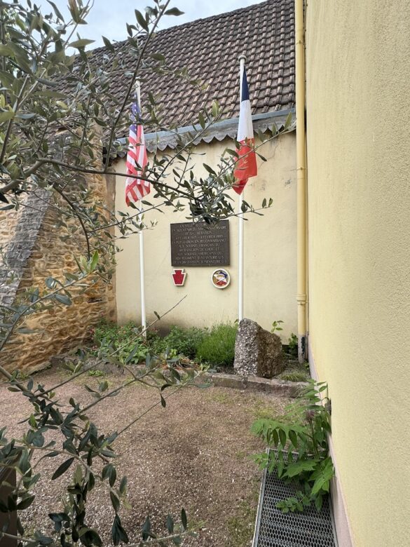 Museum sign mounted on a yellow wall with French flag and flowers in Turckheim, France.