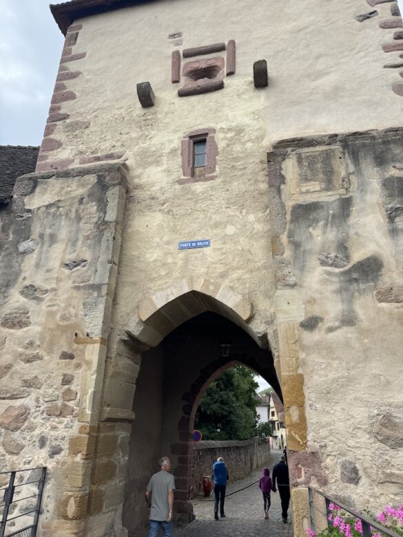 Historic stone gate tower with arched entryway and flowers at the entrance to Turckheim, France.