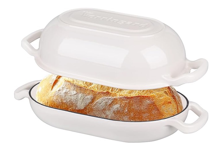 White long Dutch oven with lid lifted, showing an oval sourdough loaf baking inside