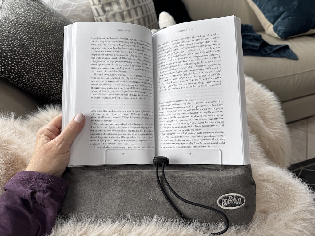 open book resting on gray bean bag book holder on a lap