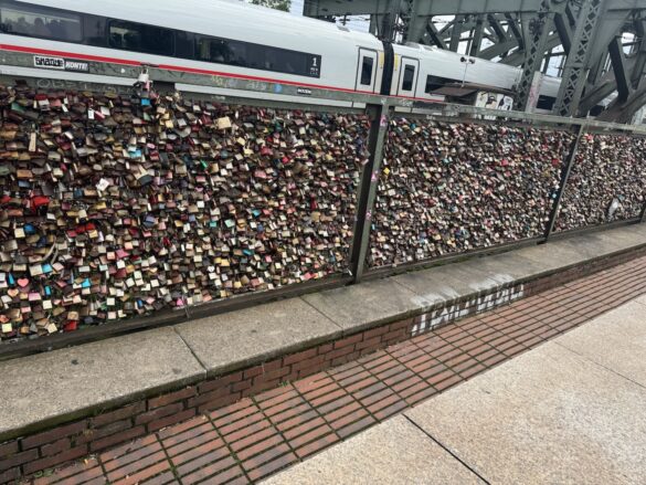 Wide view of love locks covering a section of the Hohenzollern Bridge railing with a train passing above in Cologne, Germany