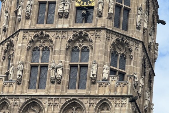 Close view of Cologne City Hall tower with Gothic stone carvings, statues, and black-and-gold clock